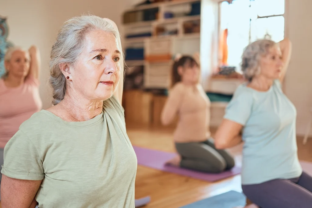 Vier Damen im präventiven Gesundheitskurs üben Dehnübungen für die Schultern aus.