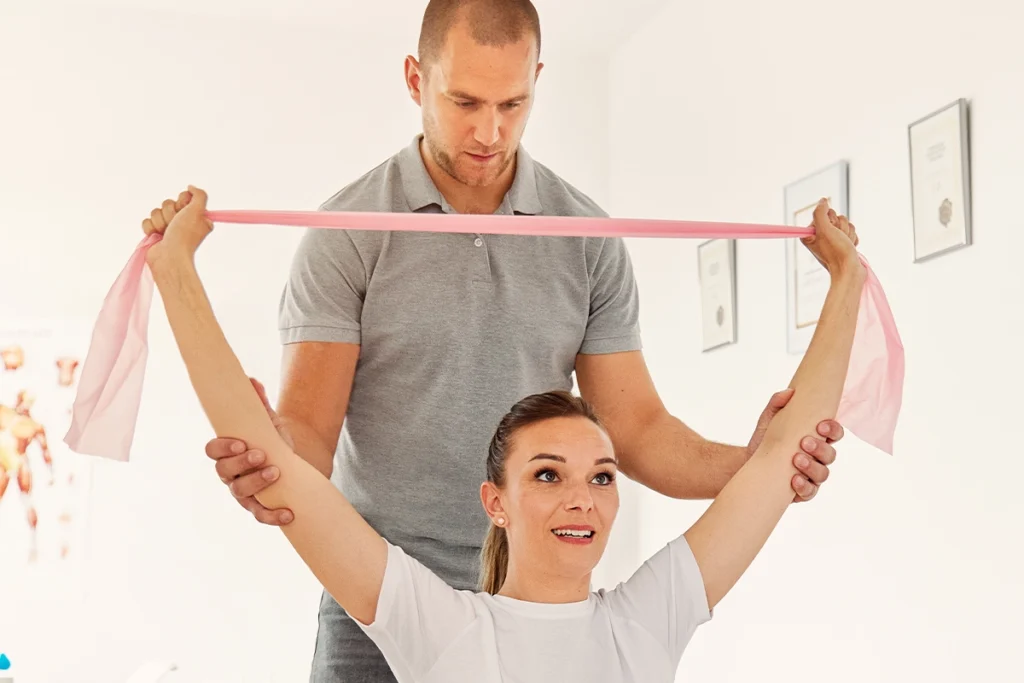 Ein Physiotherapeut hilft einer Patienten bei Armübungen mit einem Gymnastikband