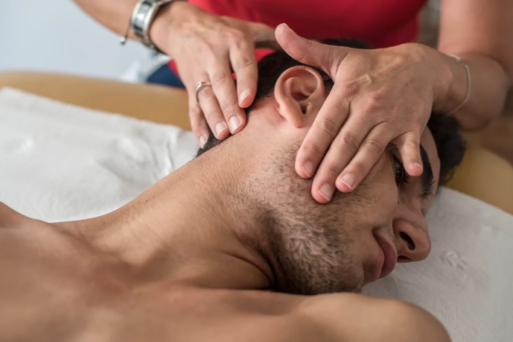 Behandlung von CMD mit Händen der Physiotherapeutin am Nacken und dem Kiefergelenk eines Patienten.