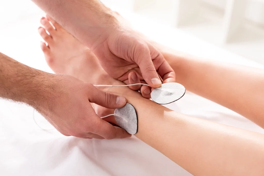 Elektroden werden am Bein eines Patienten durch den Therapeuten zur Elektrotherapie angelegt.