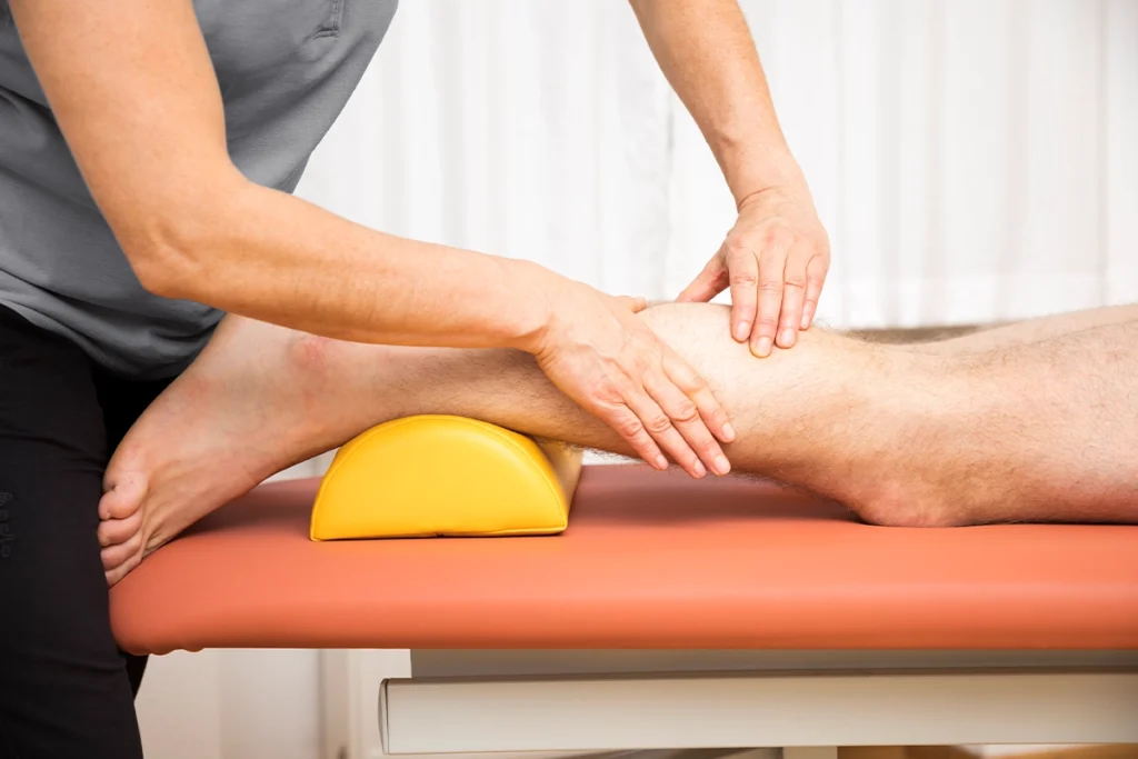 Physiotherapeutin massiert während der Krankengymnastik die Wade ihres Patienten.