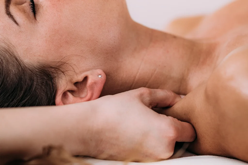 Hand der Physiotherapeutin hält Haut im Schulter-Nacken-Bereich einer Patientin während der Maasagetherapie bei trinitas.