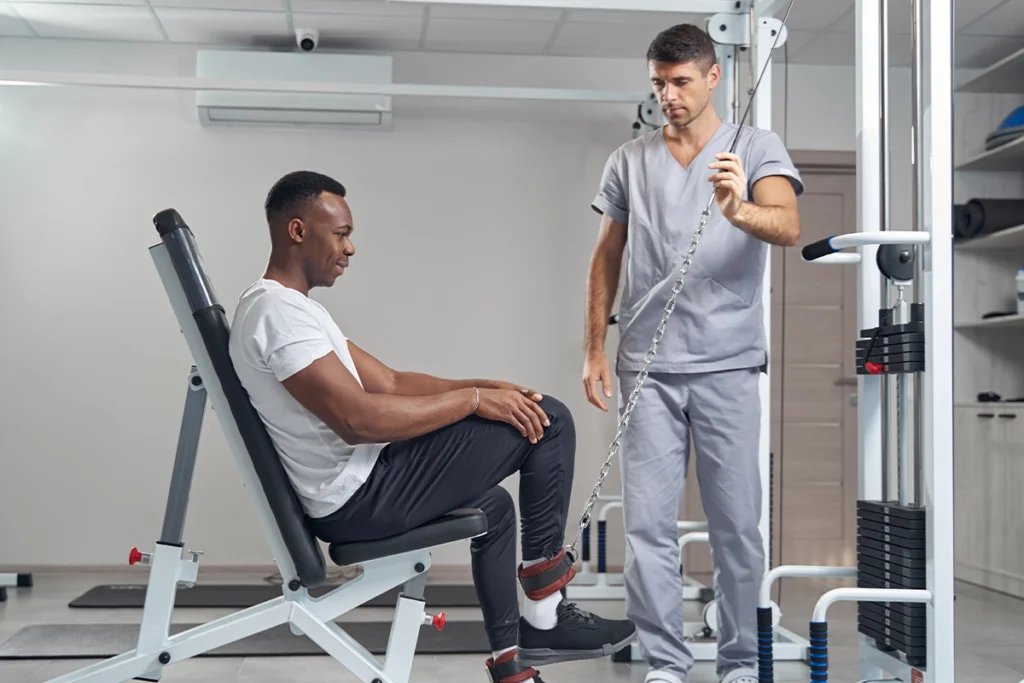 Gerätetraining in einer physiotherapeutischen Praxis: Ein Patient nutzt moderne Trainingsgeräte zur Verbesserung von Kraft und Ausdauer, unterstützt durch professionelle Betreuung durch einen Trainingstherapeuten.