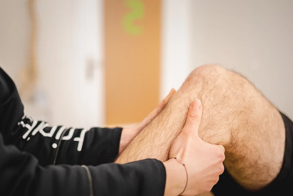 Hände einer Physiotherapeutin am Unterschenkel und Knie eines Patienten während der manuellen Therapie