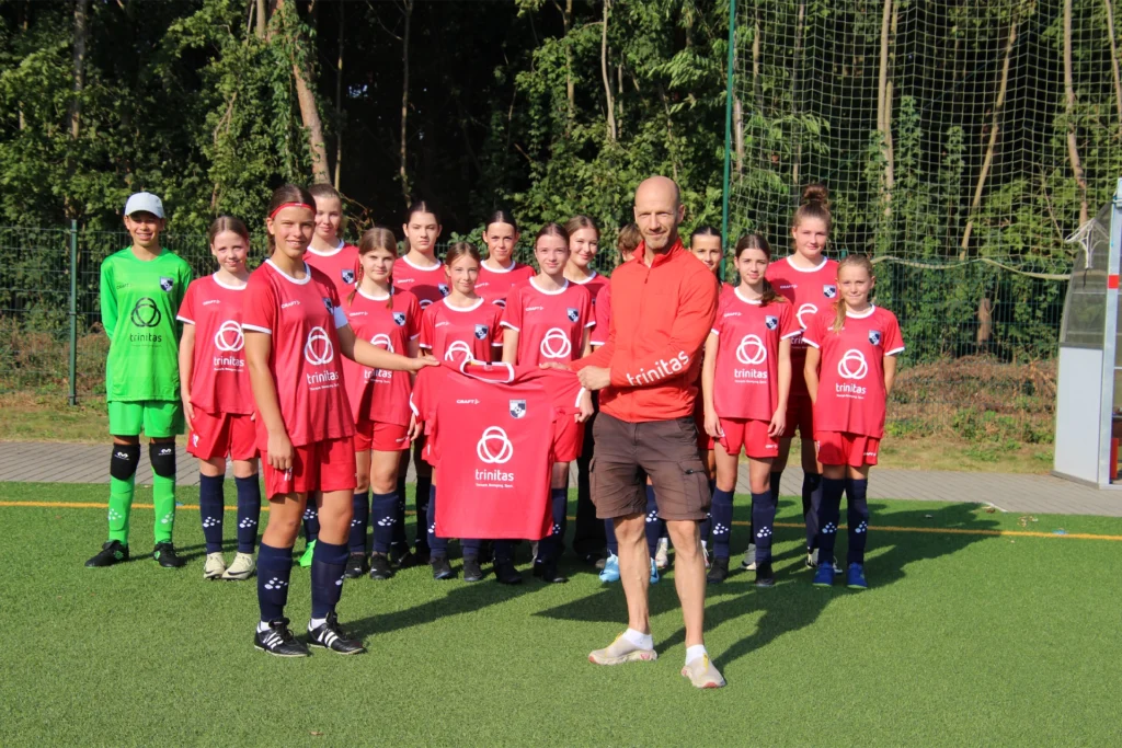 Eine Kinderfußballmannschaft mit ihrem Trainer. Alle haben T-Shirts mit dem Trinitas Logo