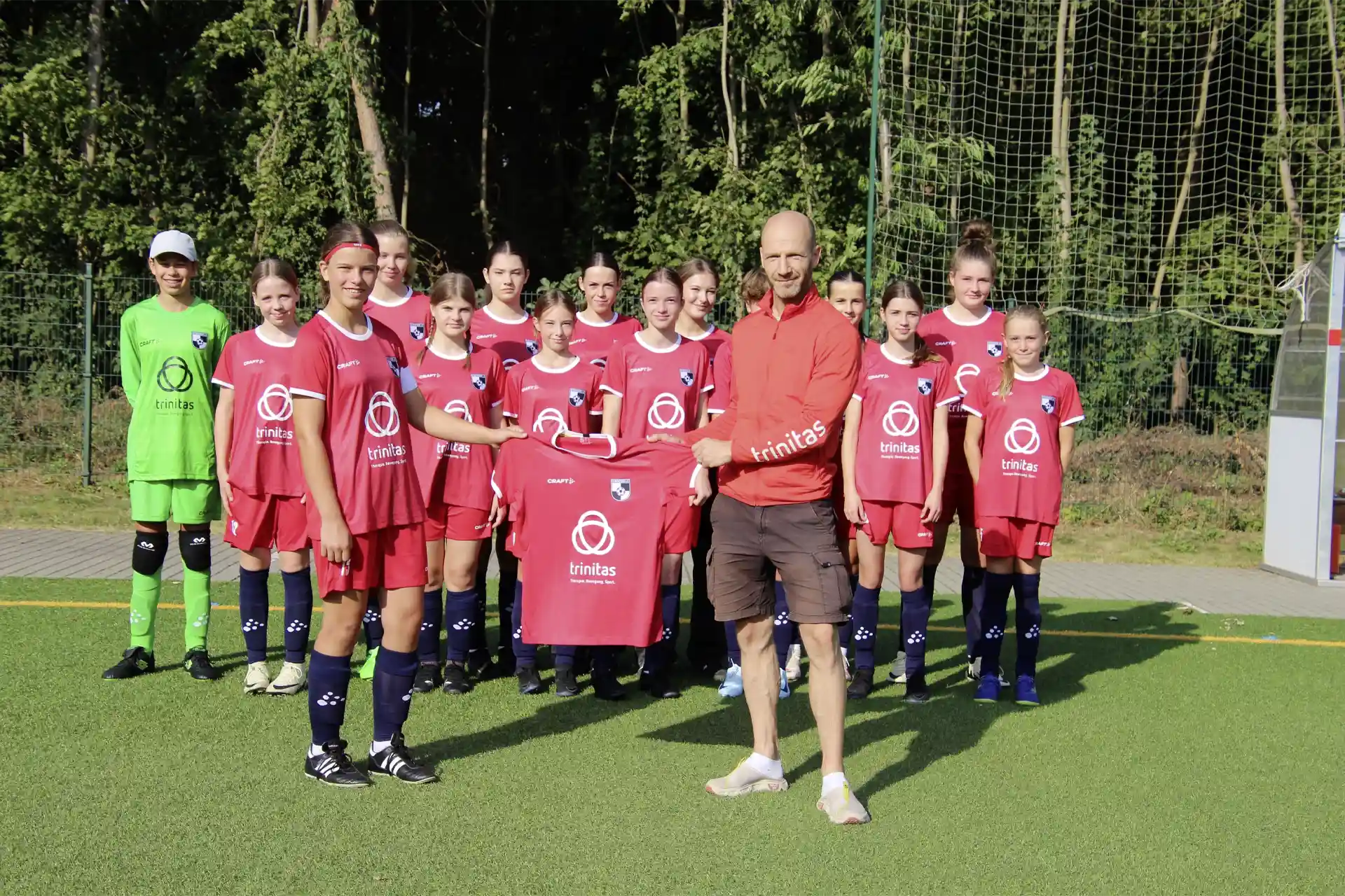 Eine Kinderfußballmannschaft mit ihrem Trainer. Alle haben T-Shirts mit dem Trinitas Logo