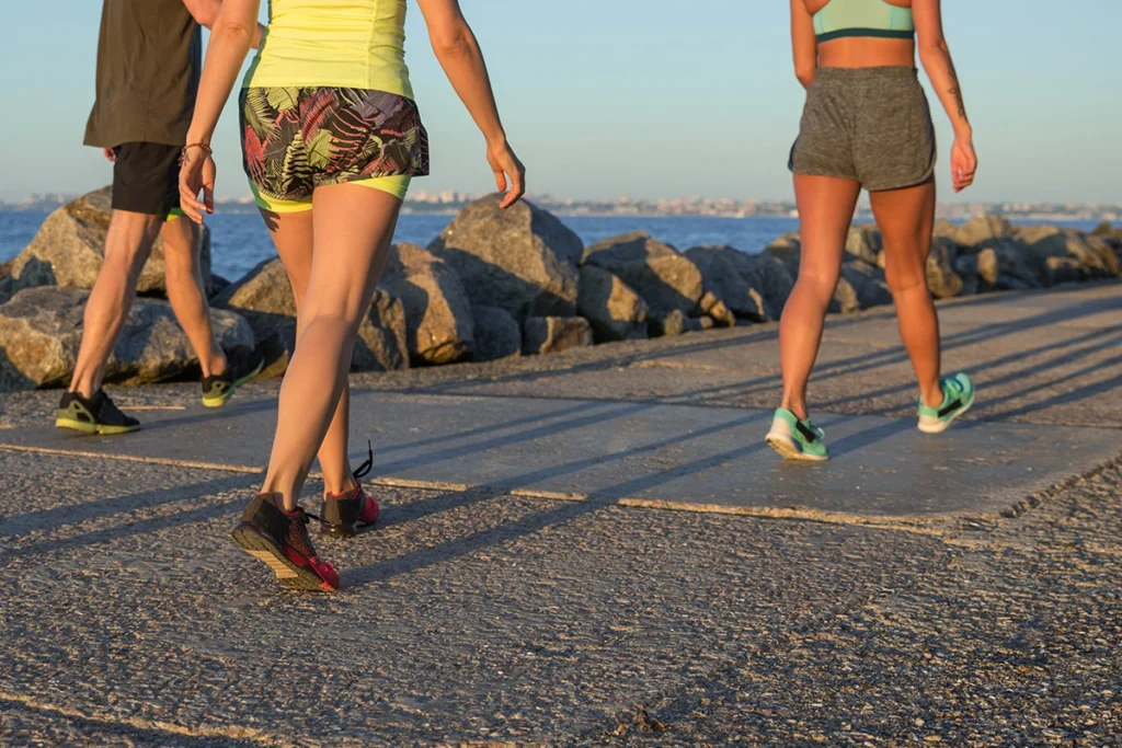 Drei Personen in Sportkleidung gehen in Joggingkleidung auf einen Beton Weg am Meer entlang